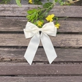 Detail einer cremeweißen Schleifen-Haarspange aus Satin mit Bändern auf rustikalem Holz - Beige