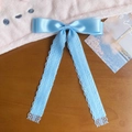Detail einer hellblauen Satin-Haarschleife mit elegantem Spitzenband auf Holztisch - Blau