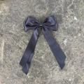 Close-up of a large black satin bow hair clip with long ribbons on a stone background - Black