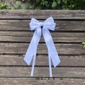 Detailed view of white satin bow hairclip with long flowing ribbons on wooden bench - White