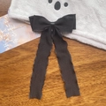 Detailed view of black pleated ribbon bow hairclip with long flowing streamers on wooden surface - Black