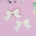 Detail view of two cream satin ribbon bow hair clips with long dovetail tails - 2-Piece Set / Beige