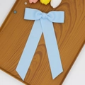 Détail d'une pince à cheveux à nœud bleu clair avec de longs rubans sur plateau en bois - Bleu clair