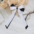 Detail of black and white satin ribbon bow hair clip with streamers on a soft plush background - Black+White