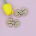 Detail view of beige grosgrain ribbon bow clips on a soft pink background with a tulip - Beige