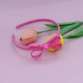 Detalle de una diadema de cinta de faya rosa con lazo delicado sobre un fondo floral - Rosa Oscuro