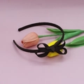 Detail view of a brown ribbed bow headband placed next to pink and yellow tulips - Coffee