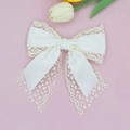 Detail view of white lace and satin bow hair clip on a soft pink background with tulips - White