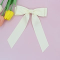 Dettaglio di un fiocco per capelli in raso crema con nastri lunghi su sfondo rosa - Metro