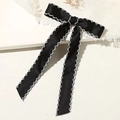 Detalle de un lazo de satén negro con elegante borde ondulado blanco y bordado - Goma de pelo / Negro