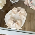 Paire de barrettes à nœuds en satin crème avec strass en cœur sur un plateau décoratif - Beige