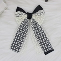 Detail of elegant black and white lace bow hair clip with ribbons on white faux fur - Black