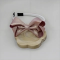 Primer plano de diadema con lazo rosa en capas y acabado perlado en soporte de madera - Rosa
