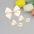 Macro detail of elegant cream pleated ribbon hair clips in three sizes with silk texture - Beige