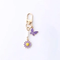 Golden butterfly keychain with purple flower and pearls hanging on a white background - Purple Butterfly And Flower Style (海星蝴蝶)