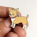 Gros plan d'une broche carlin en émail jaune et blanc tenue à la main pour comparer la taille - Style Chihuahua Jaune