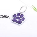 Macro shot of purple glitter paw-shaped pet ID tag with a heart detail and metal split ring - Purple