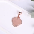 Makroaufnahme eines roségoldenen Herzanhängers mit glitzernden Strasssteinen und Glöckchen - Roségold + Glocke