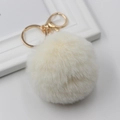 Close-up of fluffy white faux fur pompom keychain with elegant golden metal lobster clasp - Off-white