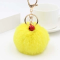 Dettaglio di un pompon in ecopelliccia gialla con campanellino rosso e gancio dorato - Giallo