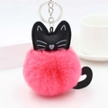 Close-up of pink fluffy cat pompom keychain with black leather details on a white table - Watermelon red