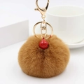 Nahaufnahme brauner Kunstpelz-Schlüsselanhänger mit goldener Hardware und roter Glocke - Kaffeebraun