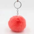 Detail view of a fluffy coral pink pompom keychain with a polished silver metal ring - Orange Red