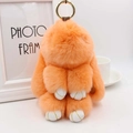Porte-clés lapin géant en fourrure orange avec anneau doré sur décor de maison cosy - Orange