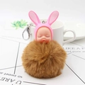 Close-up of sleeping baby doll keychain with pink bunny ears and soft brown fur pompom - Coffee