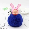 Close-up of fluffy blue pom-pom keychain with a sleeping doll in a pink bunny hat - Sapphire Blue