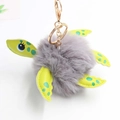 Close-up of plush turtle keychain with grey faux fur ball and green spotted limbs - Pom Pom Diameter 8cm / Light Gray