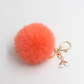 Close-up of bright orange faux fur pom pom keychain with gold clasp and rainbow charm - Orange Red