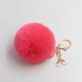 Detailed macro view of a fluffy pink faux fur pompom keychain with golden rainbow charm - Watermelon red