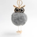 Macro detail of plush owl keychain with gray faux fur ball and golden metal owl head charms - Medium Grey
