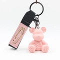 Detail eines rosa Bärenanhängers mit Webstruktur, schwarzem Band und Goldaufdruck - Rosa