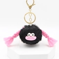 Detail view of a black fluffy monster keychain with pink braids and big eyes on white base - Black