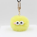 Gros plan d'un porte-clés pompon jaune avec yeux de dessin animé et fermoir doré - Jaune