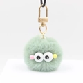 Détail d'un porte-clés pompon vert clair avec de grands yeux et clip doré - vert clair