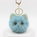 Close-up of light blue plush cat keychain with green ears on a white display stand - Lake Blue