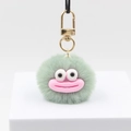 Detail of green plush pompom keychain with big eyes, pink mouth and golden metal clasp - Light Green