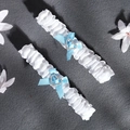 Close-up of white lace bridal garters with blue satin bows and heart crystal accents - One Size / GS-J024 Style