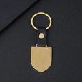 Llavero de escudo metálico dorado con correa de cuero negro sobre fondo oscuro texturizado - Forma de Escudo / Estilo de Cuero Dorado