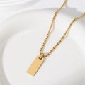 Close-up of a polished gold rectangular bar pendant on a box chain over a white plate - 25X10mm Rectangle With Box Chain / Gold