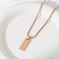 Detailed view of rose gold bar pendant on a box chain placed on a white ceramic dish - 25X10mm Rectangle With Box Chain / Rose Gold