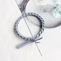 Elastico per capelli intrecciato grigio chiaro con nappa decorativa su sfondo testurizzato - Celeste