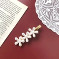 Detalle de una elegante horquilla dorada con tres flores de perlas sobre un fondo rojo oscuro - Estilo de 3 Flores