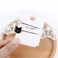 Detailansicht der Perlen-Katzenpfote und schwarzen Emaille-Haarspangen in der Hand - Schwarzgesicht Katze