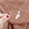 Close-up of golden hollow heart hair clip with three white pearls and sparkling zircon - Heart