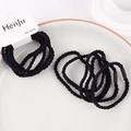 Detail of black braided hair ties on a ceramic tray showing elastic spiral texture - Plait Black