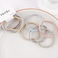 Detail of braided macaron elastic hair bands on a beige ceramic plate with brand tag - Plait Mixed Colors